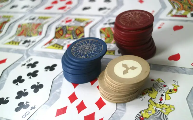 Stacks of blue, red and cream casino chips resting on a spread of playing cards